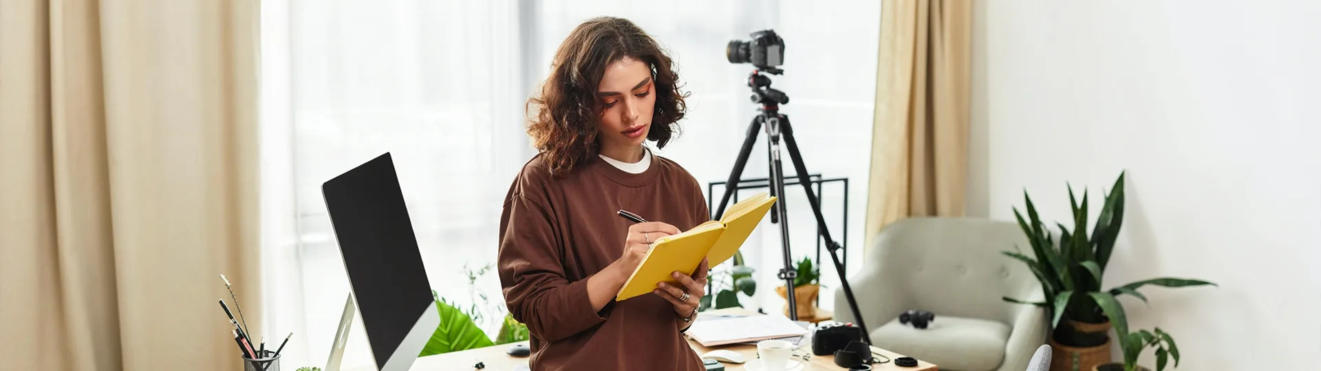 Creator writing in a yellow notebook in a bright home studio with a camera on a tripod behind her