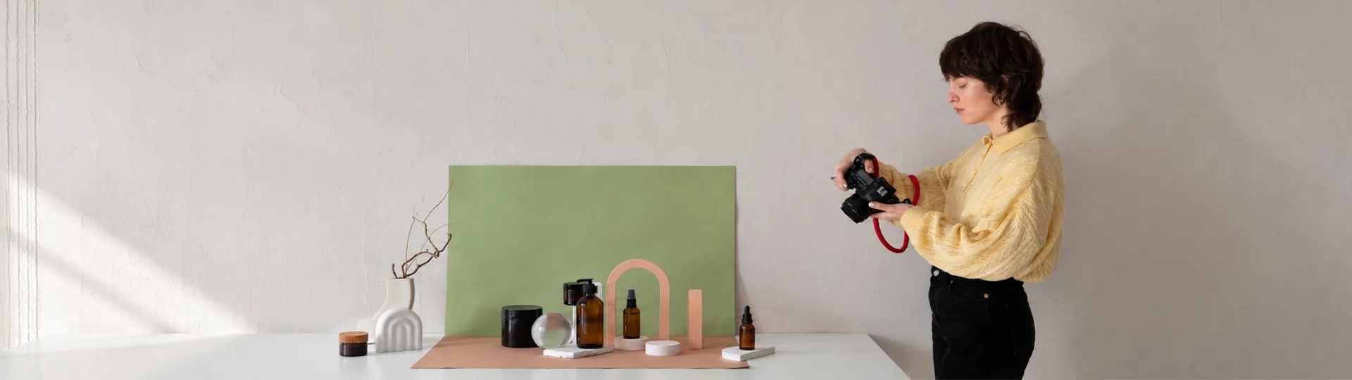 Photographer checking her camera beside a styled skincare product set on a green backdrop