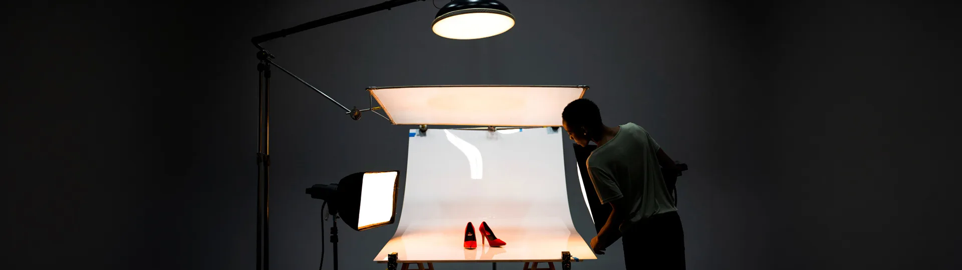 Photographer adjusting studio lights around a pair of red high heels on a white backdrop