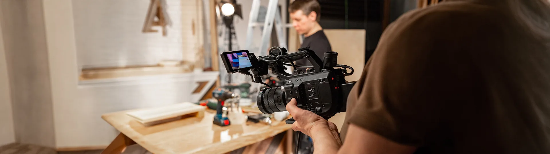 Camera operator filming a woodworking scene on set with a professional video camera and studio lighting