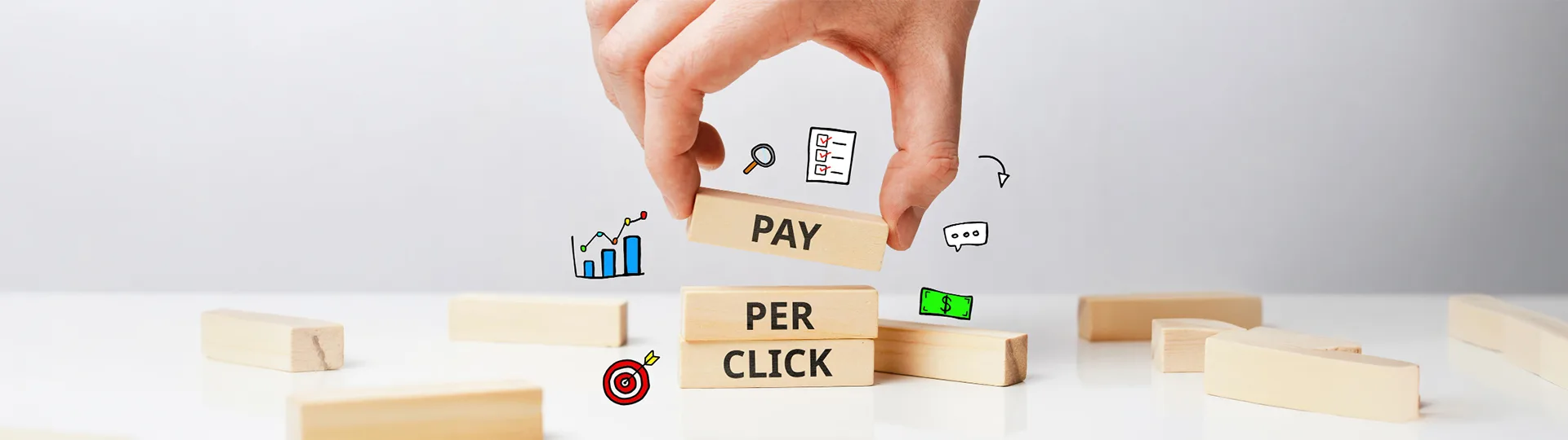 Hand stacking wooden blocks that spell Pay Per Click, surrounded by sketched chart and target icons
