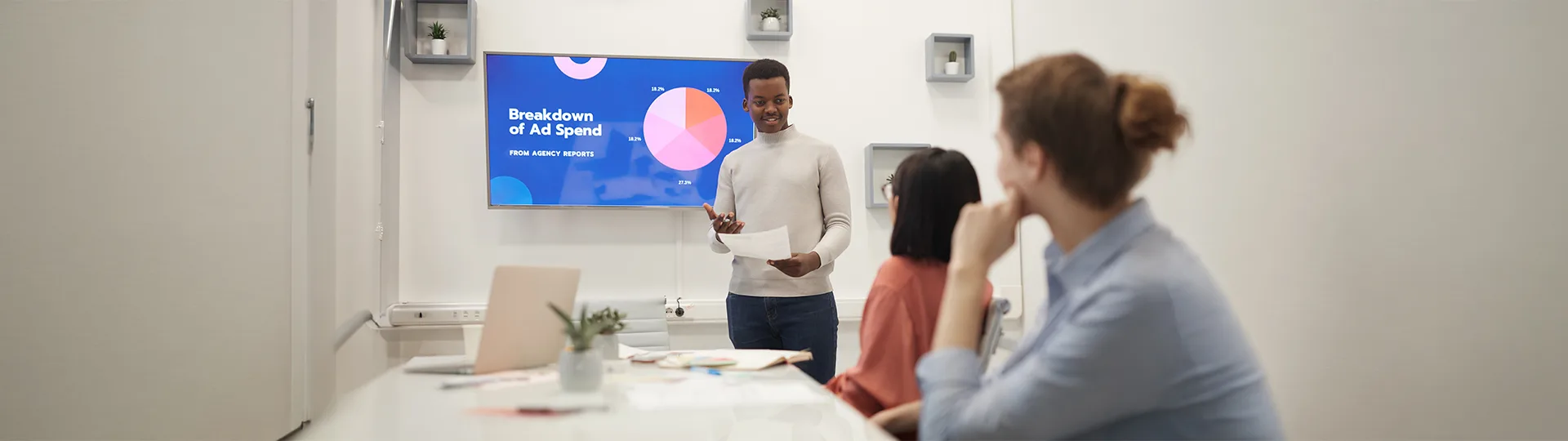 Team member presenting a Breakdown of Ad Spend chart to colleagues in a meeting room
