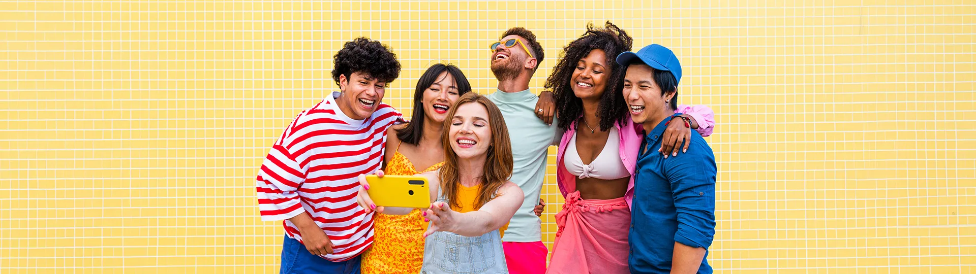 Group of young friends laughing and taking a selfie in front of a yellow tiled wall
