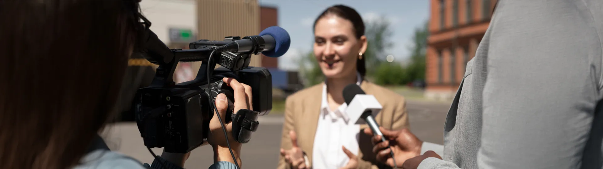 Businesswoman giving an outdoor interview to a reporter holding a microphone and a camera operator filming