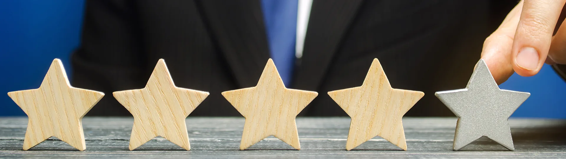 Businessman placing a silver fifth star at the end of a row of four wooden stars