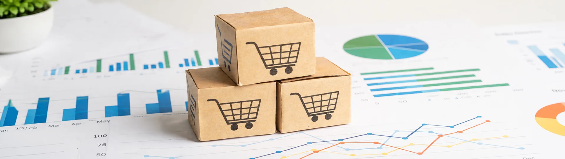 Cardboard boxes printed with shopping cart icons stacked on sales charts and graphs