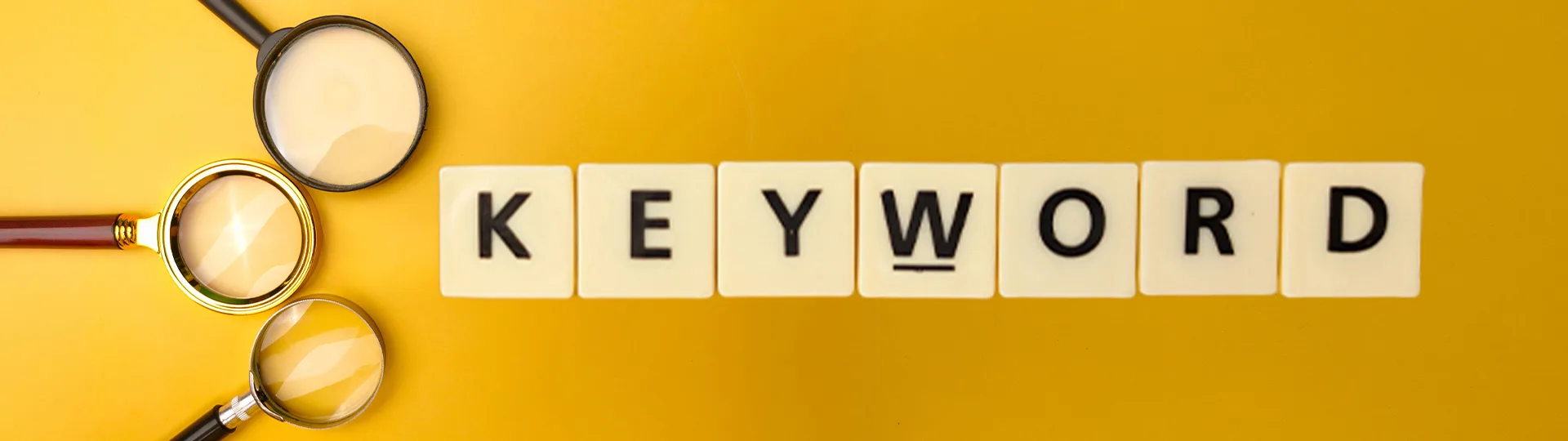 Letter tiles spelling Keyword beside three magnifying glasses on a yellow background