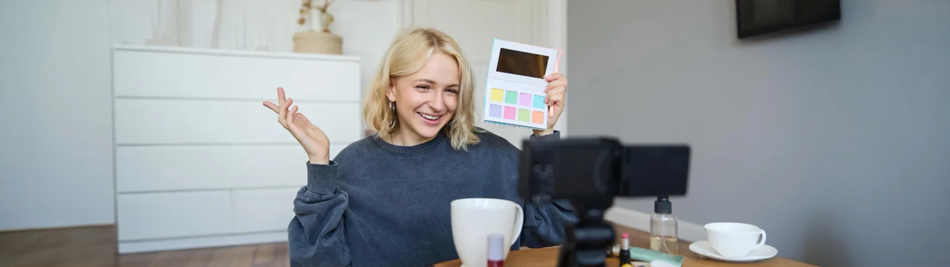 Beauty creator smiling and holding up an eyeshadow palette while recording a review on camera