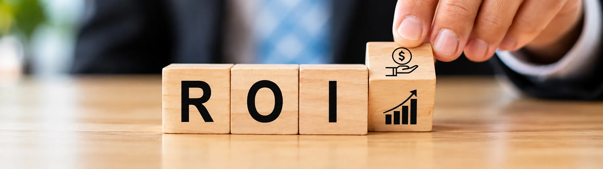 Hand placing a wooden block with money and growth chart icons next to blocks spelling ROI
